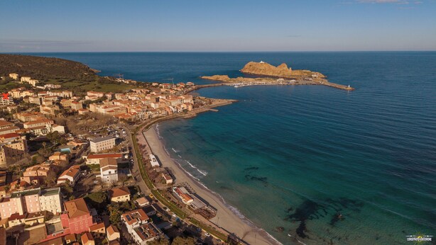 Vista aérea de un pueblo costero con playa, edificios y una estructura similar a una fortaleza.