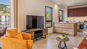 Una sala moderna con un televisor de pantalla plana grande, un sofá con cojines naranja y una mesita redonda con un frutero.