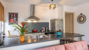 Une cuisine moderne avec un réfrigérateur en acier inoxydable, une cuisinière à gaz et un grand îlot central doté d’un évier. On trouve une plante en pot sur l’îlot et un saladier de fruits sur le plan de travail.