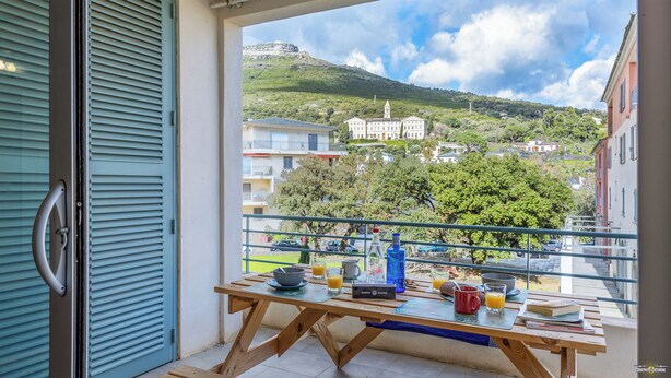 Un balcon avec une table dressée pour le petit-déjeuner, donnant sur une colline parsemée de bâtiments et de verdure.