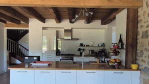 Een moderne keuken met een groot eiland, witte kasten en een accentmuur van steen.