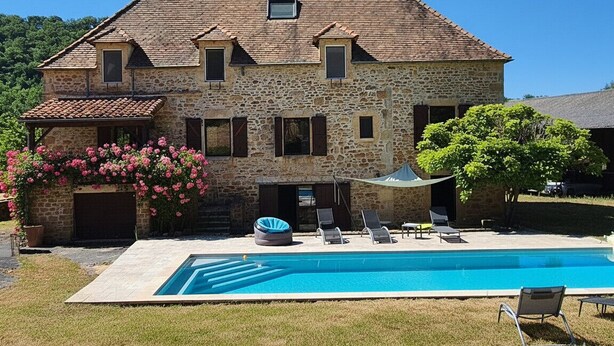 Een stenen huis met een zwembad, terras en tuin.