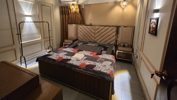 A bedroom with a bed, a ceiling fan, an air conditioning unit, and a bedside table.
