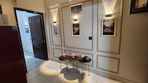 A hallway with a reception desk, framed artwork, and a door leading to another room.