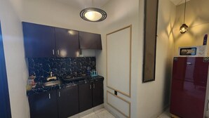 A kitchen with dark cabinets, a marble countertop, a refrigerator, and a pendant light.