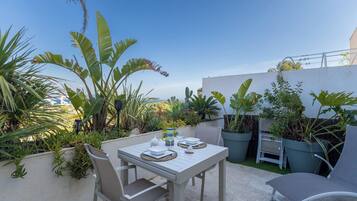 An outdoor patio with a table set for two, surrounded by potted plants and a clear sky.