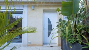 Un edificio con una puerta blanca, un ventanal pequeño y una maceta con plantas.