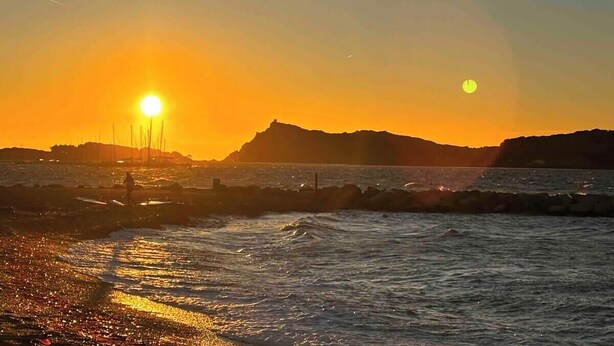 Atardecer sobre una zona costera con costa rocosa y una colina distante.