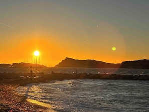 A sunset over a coastal area with a rocky shoreline and a distant hill. - T2 avec Terrasse à Six-Fours - Piscine + Parking (Six-Fours-les-Plages)