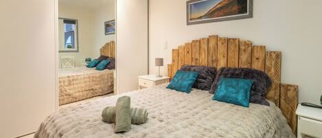 Een slaapkamer met een groot bed, een houten hoofdbord, een spiegel en een schilderij aan de muur.