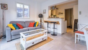 Una sala de estar moderna con un sofá gris, cojines coloridos, una mesa de centro de vidrio y un sillón blanco.