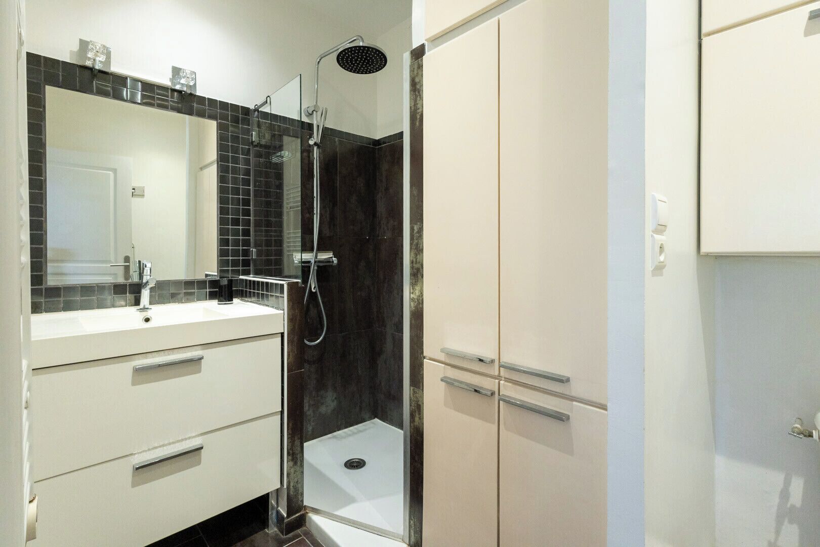 Een moderne badkamer met een glazen douchecabine, een wit wastafelmeubel en een grote spiegel.