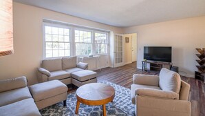 A spacious living room with a sectional sofa, a round coffee table, and a flat-screen TV. - The Marsh House (Brunswick)