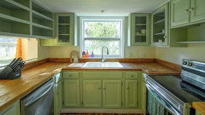 A kitchen with green cabinets, a wooden countertop, a sink, and a stove. - The Marsh House (Brunswick)
