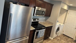 Eine moderne Küche mit Edelstahlgeräten, dunklen Holzschränken, Granitarbeitsplatten, einem eingebauten Backofen, einer Mikrowelle und einer Waschmaschine.