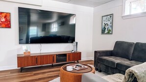 Un salon moderne avec un téléviseur à écran plat fixé au mur, un canapé en cuir foncé, une table basse en bois et un tapis blanc.