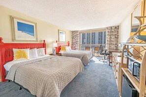 Ett hotellrum med två sängar, ett skrivbord, en stol, ett stort fönster med utsikt över höga byggnader och en mikrovågsugn.