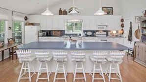 A spacious kitchen with white cabinets, a large island with bar stools, pendant lighting, and a view of the outdoors. - Well-appointed 5-bedroom, 5 bathroom house on gorgeous Lake Wateree with AC (Ridgeway)