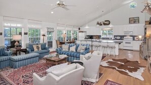A spacious living room with a large sofa set, a coffee table, and a patterned rug. There is a kitchen area with white cabinets and a dining table with bar stools. - Well-appointed 5-bedroom, 5 bathroom house on gorgeous Lake Wateree with AC (Ridgeway)