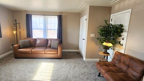 A living room with a brown leather sofa, a small side table, a floor lamp, and a potted plant. - Comfortable 2BR Near Lakewalk with Private Entry & Parking (Duluth)