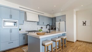 Eine moderne Küche mit hellblauen Schränken, einer weißen Arbeitsplatte und einer zentralen Kochinsel mit Sitzgelegenheiten.