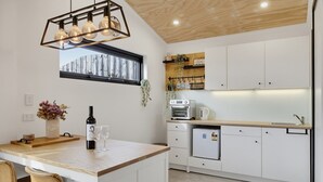 Una cocina moderna con techo de madera, horno empotrado, refrigerador y ventana con vista a una construcción de madera.