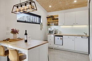 Eine moderne Küche mit Holzboden, Backofen, Kühlschrank und einem Fenster mit Blick auf ein Holzgebäude.