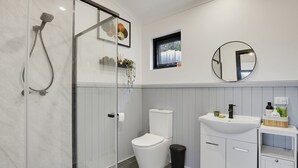 A modern bathroom with a glass shower enclosure, a toilet, a sink with a mirror, and a small window. - The Studio | A Slower Stay in Normanville | 5 Mins to the Beach (normanville)
