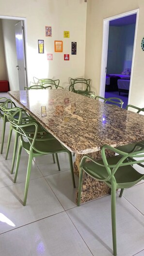 Un coin repas avec une table en granit et des chaises vertes, une porte donnant sur une chambre et des éléments décoratifs sur les murs.