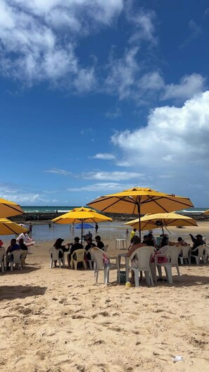 A beach with yellow umbrellas and white plastic chairs. - Family beach house (Cabo de Santo Agostinho)