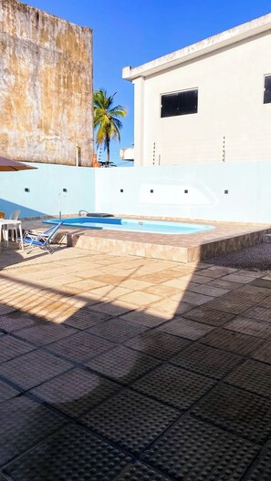 A rooftop swimming pool with a clear blue sky, a palm tree, and a building in the background. - Family beach house (Cabo de Santo Agostinho)