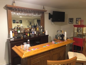 A bar area with a wooden counter, various bottles, glasses, and a TV mounted on the wall. - Caribbean Deck Estate The Poconos Best Kept Secret. (Effort)