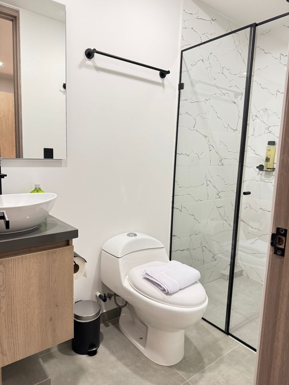 Un baño moderno con inodoro blanco, lavamanos con espejo y cabina de ducha de vidrio.