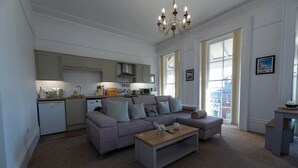 A modern living room with a grey sofa, a coffee table, and a kitchen area with light-colored cabinets and a dishwasher. - Spacious 2 Bed Apartment in Brighton with Parking (Brighton and Hove)
