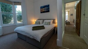 A bedroom with a large bed, a nightstand, a painting, and a view of the outdoors through a window. - Spacious 2 Bed Apartment in Brighton with Parking (Brighton and Hove)