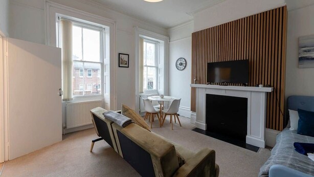 Un salon moderne comprenant un canapé, une cheminée, un téléviseur et un coin repas avec des chaises.