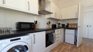 A compact kitchen with white cabinets, a microwave, a washing machine, and a small oven.