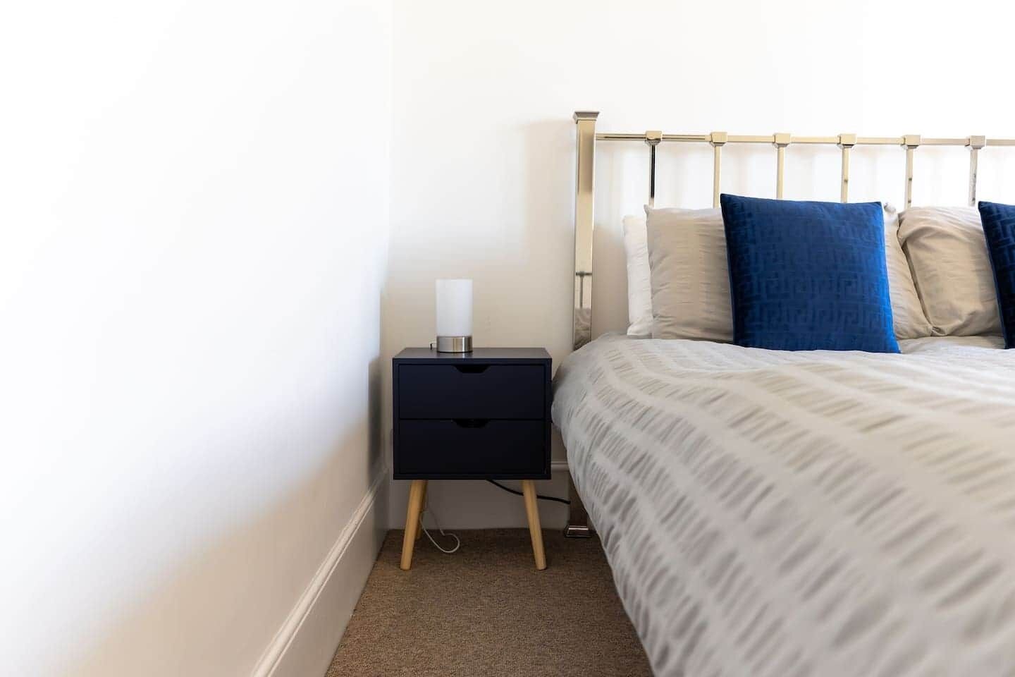 A neatly made bed with a patterned bedspread, a bedside table with a lamp, and a wall-mounted headboard.