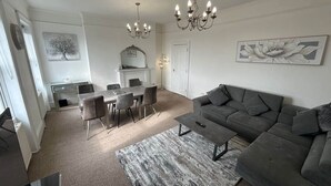 A modern living room with a grey sofa, a dining table with chairs, and a chandelier.