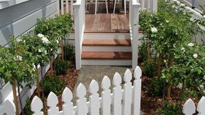 A wooden deck with white picket fencing, a white umbrella, and a white fence.