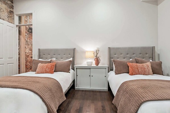 Habitación doble con dos camas, una mesita de noche con lámpara y una pared de ladrillo.