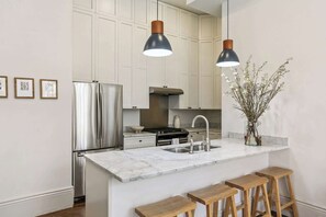 A modern kitchen with a central island, stainless steel appliances, pendant lighting, and a vase with branches.