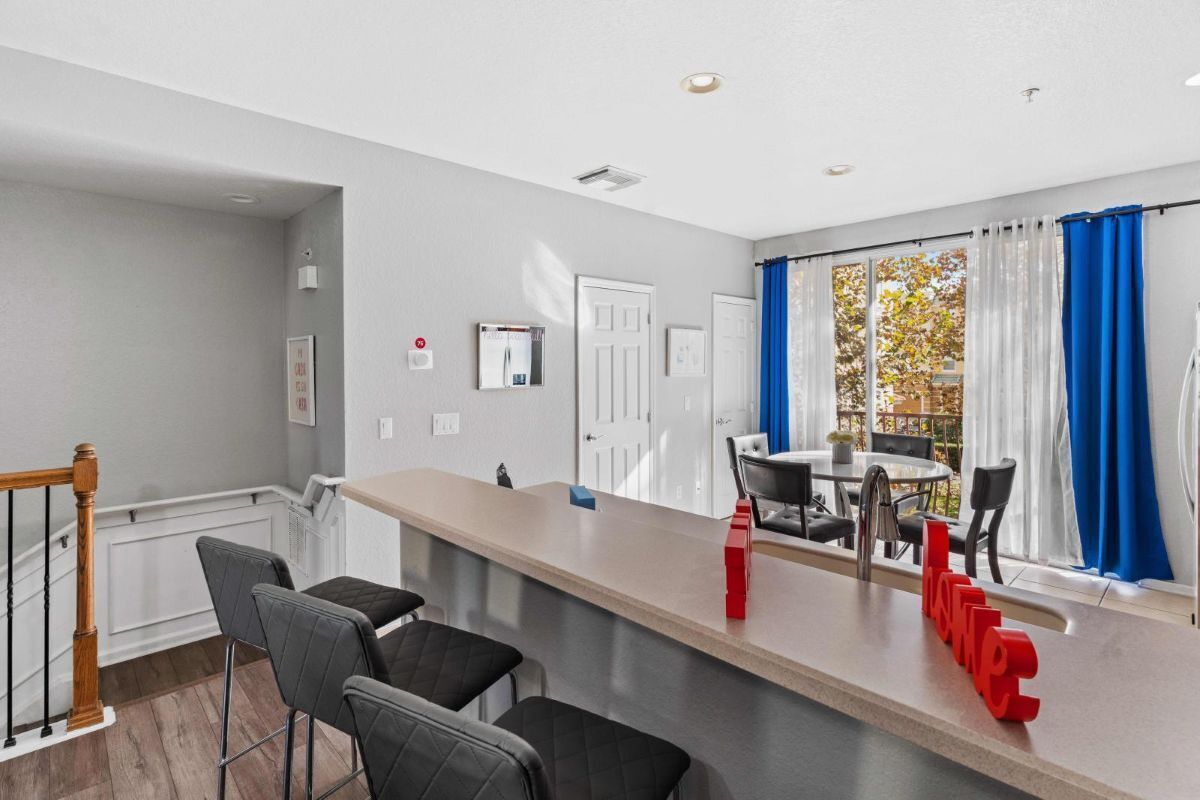 A modern kitchen with a bar area, a dining table with chairs, and a view of the outdoors through large windows.