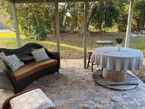 An outdoor patio with a wicker sofa, a round table, and a stone-tiled floor. - Fabulous Country Apartment in "America's Happiest Seaside Town." (Stuart)