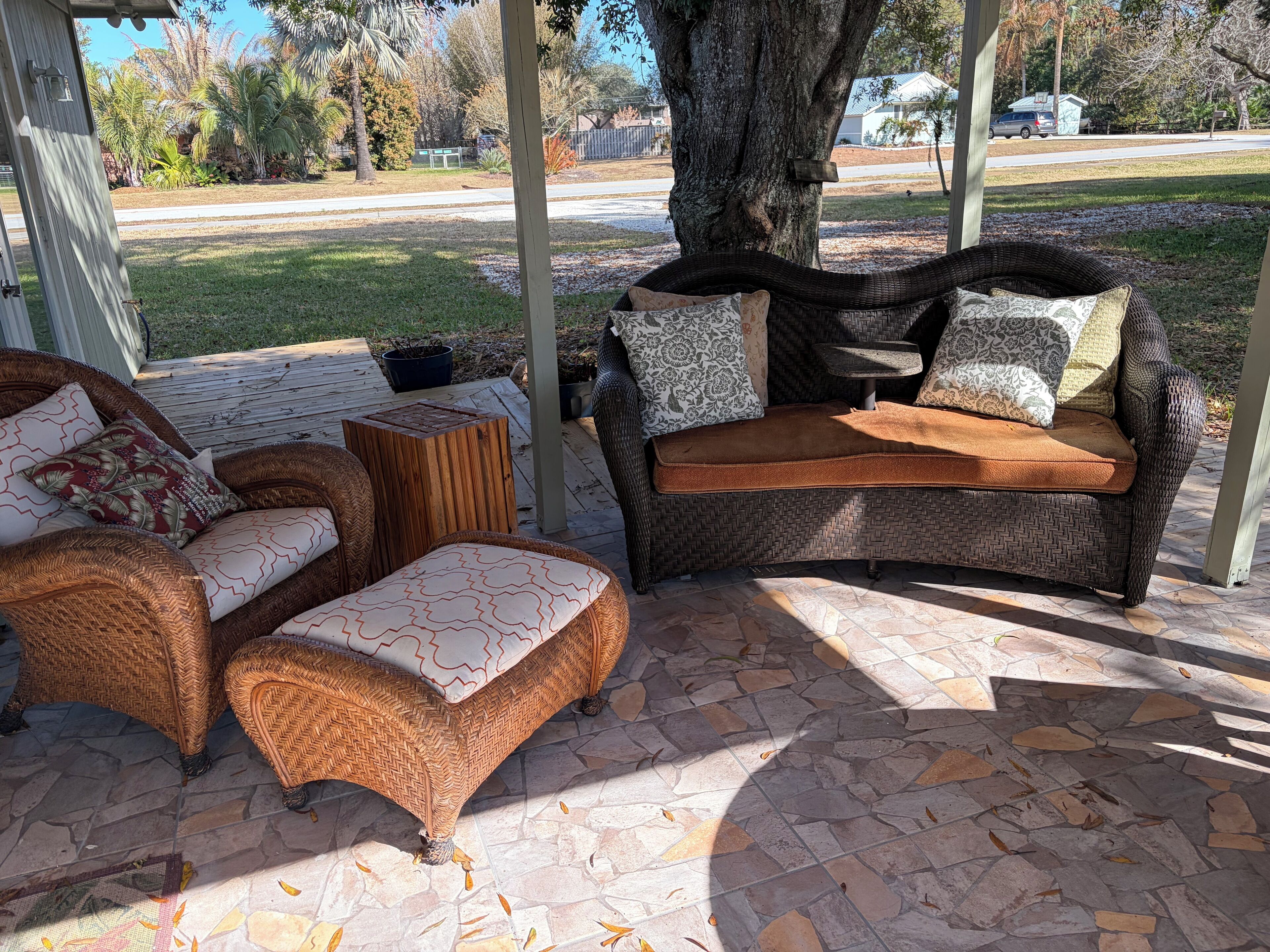 Een terras buiten met rieten meubilair, waaronder een bank en poef, en een kleine tafel.
