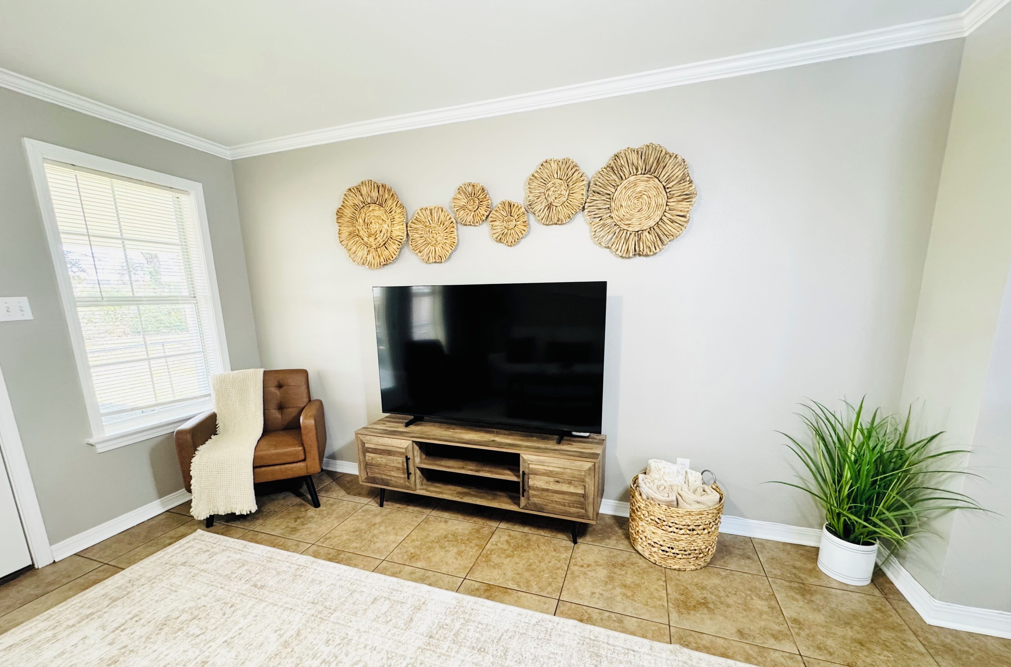 Un salón con televisor sobre un mueble de madera, un sillón de cuero marrón, alfombra color beige, una planta en maceta y decoración en la pared.