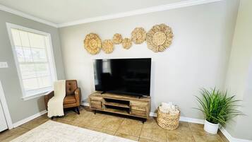 Un salón con televisor sobre un mueble de madera, un sillón de cuero marrón, alfombra color beige, una planta en maceta y decoración en la pared.