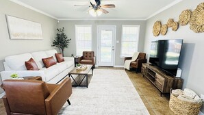 Ein Wohnzimmer mit einem weißen Sofa, braunen Ledersesseln, einem Couchtisch, einem Fernseher und einem Deckenventilator.