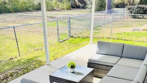 Ein überdachter Außenbereich mit Rattan-Sofa und Glastisch.