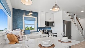 A modern kitchen with white cabinets, a blue backsplash, stainless steel appliances, and a central island with seating. - High Point Hideaway on the Sand Dunes - Unit 2 (Dauphin Island)